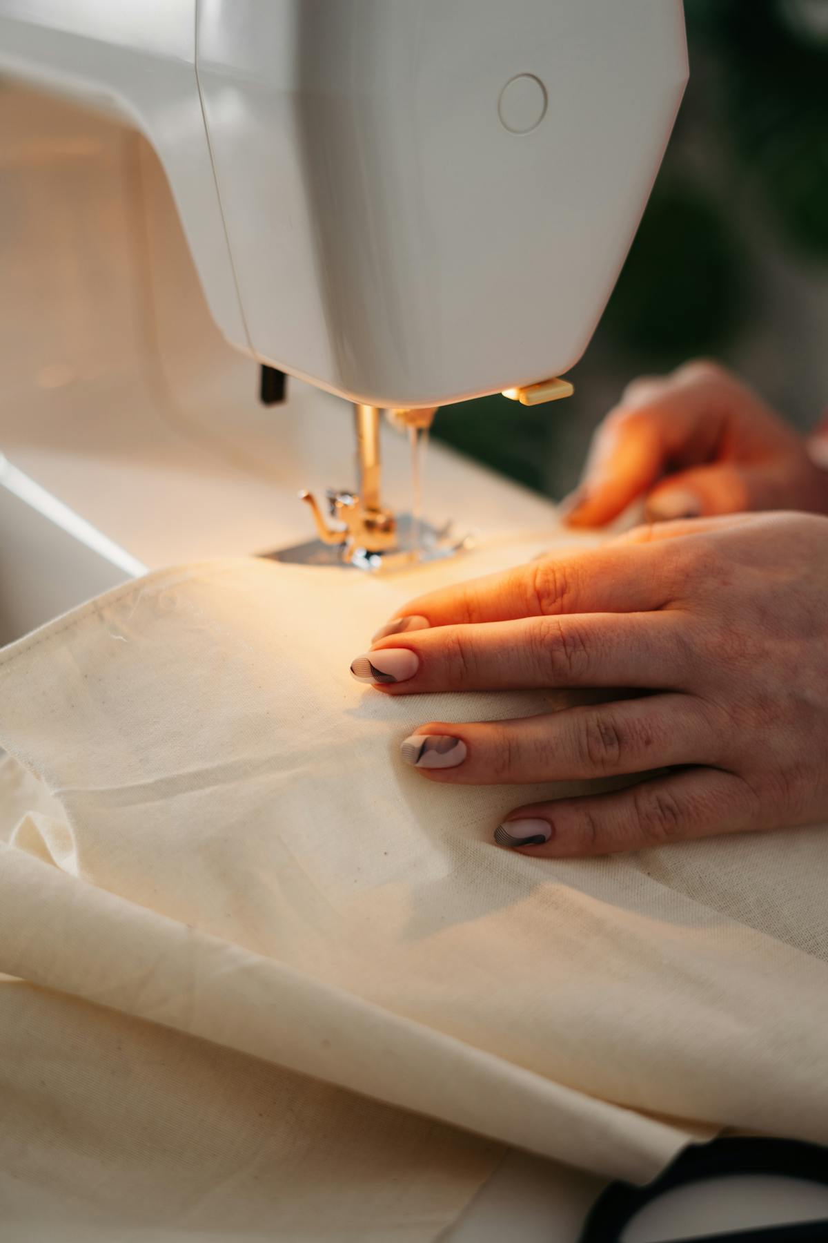 Hands stitching cream linen on a sewing machine