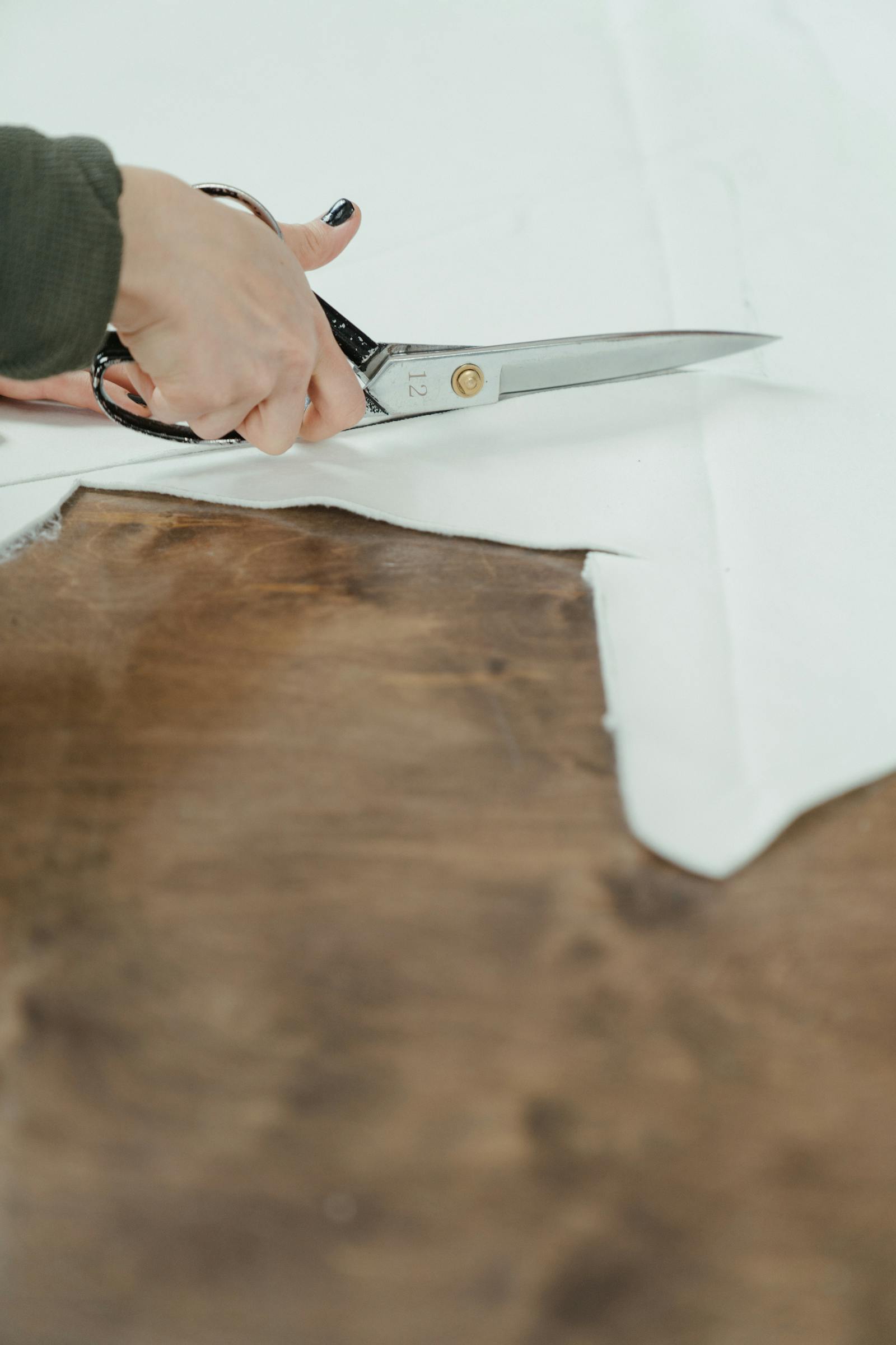 Hands cutting white linen on a dark wood table with tailoring shears